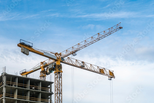 Building construction site. 2 yellow tower cranes against blue sky.