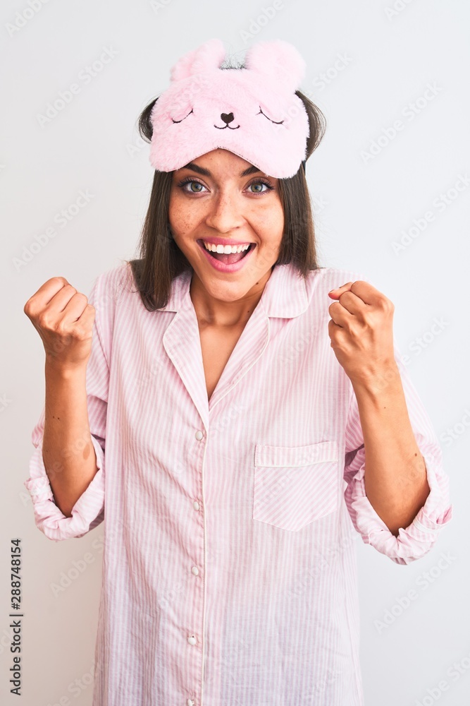 Young beautiful woman wearing sleep mask and pajama over isolated white background screaming proud and celebrating victory and success very excited, cheering emotion Young beautiful woman wearing sleep mask and pajama over isolated white background screaming proud and celebrating victory and success very excited, cheering emotion