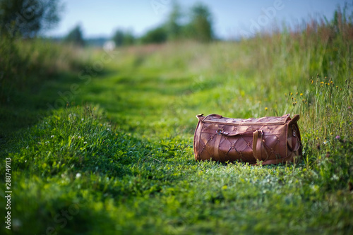 orange leather bag on a country road on a summer evening. Green grass and vegetation around the bag. copy space