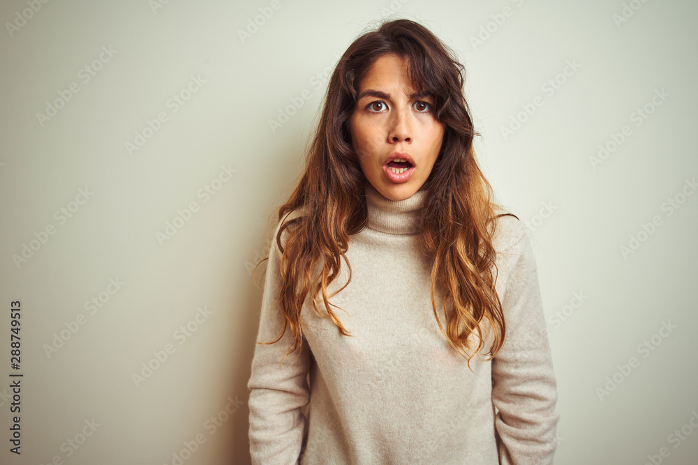 Fototapeta premium Young beautiful woman wearing winter sweater standing over white isolated background afraid and shocked with surprise and amazed expression, fear and excited face.