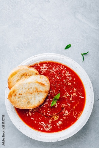 Tomato basil soup with parmesan cheese and bread toasts on gray stone background