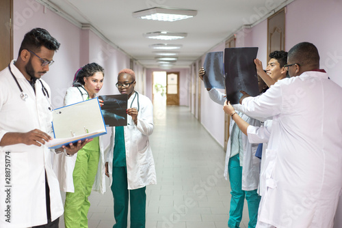 a team of young doctors. A group of people of different races, of different sexes, dressed in medical clothes, in the corridor of the hospital, looking at an x-ray, discussing medicine