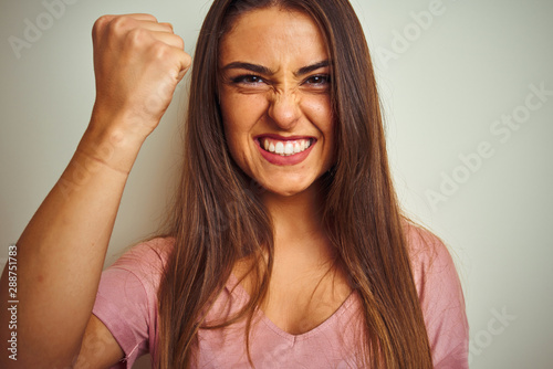 Young beautiful woman wearing pink t-shirt standing over isolated white background annoyed and frustrated shouting with anger, crazy and yelling with raised hand, anger concept