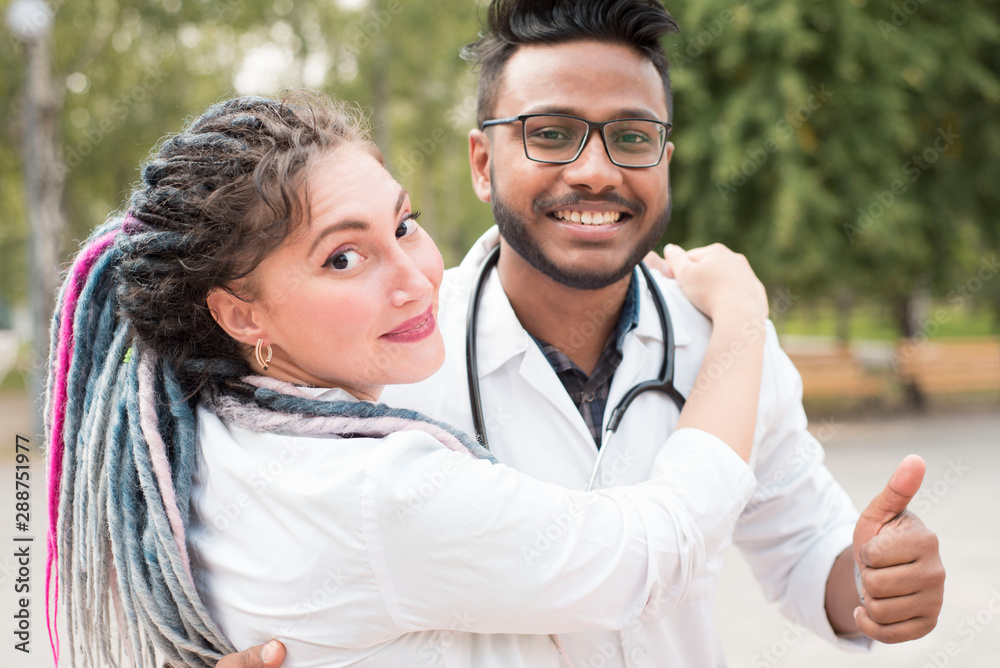 young doctors Happy people, Indian guy and white girl with dreadlocks. In white coats, phonendoscopes, on the street, hugging, laughing young doctors Happy people, Indian guy and white girl with dreadlocks. In white coats, phonendoscopes, on the street, hugging, laughing