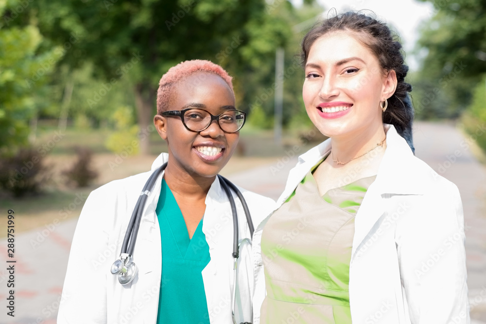 a pair of young doctors. Medical students laugh at white coats and with a stethoscope. Outdoor a pair of young doctors. Medical students laugh at white coats and with a stethoscope. Outdoor