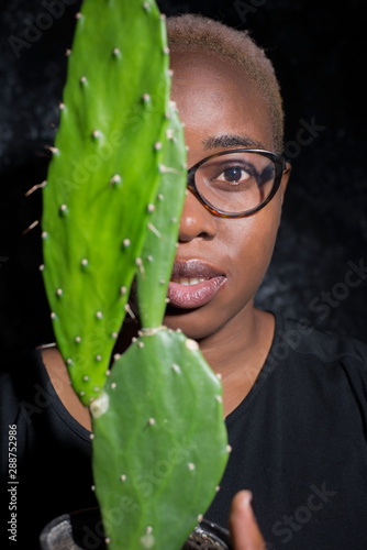 portrait of an african girl in glasses. Half of the face is covered by a cactus photo