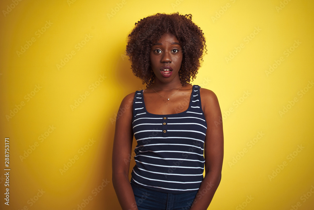 Young african afro woman wearing striped t-shirt over isolated yellow background afraid and shocked with surprise expression, fear and excited face. Young african afro woman wearing striped t-shirt over isolated yellow background afraid and shocked with surprise expression, fear and excited face.