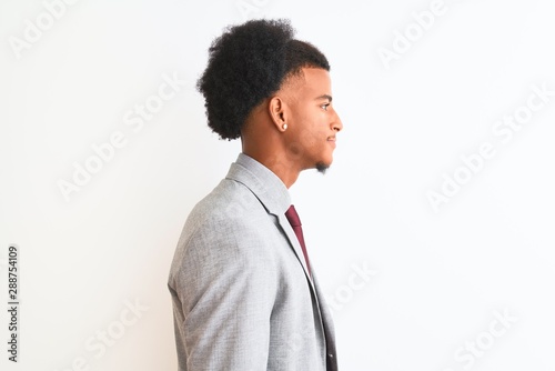 Young african american businessman wearing suit standing over isolated white background looking to side, relax profile pose with natural face with confident smile.
