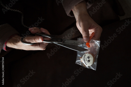 Hands cutting pack of cookies for Halloween with scissors