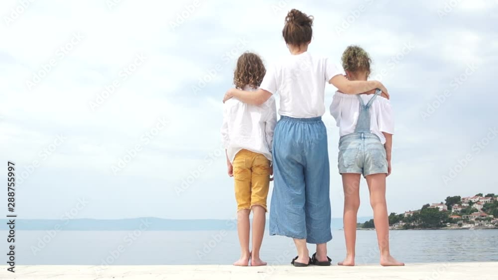 Happy family vacation, mothers day, dressed in denim, blue jeans. Mom and her two teenage children stand on the shore of the Mediterranean Sea Happy family vacation, mothers day, dressed in denim, blue jeans. Mom and her two teenage children stand on the shore of the Mediterranean Sea