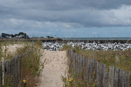 Path through the dunes to reach the seaside with boats