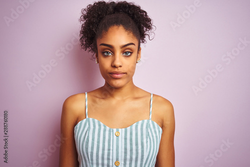 African american woman wearing casual striped dress standing over isolated pink background with a confident expression on smart face thinking serious