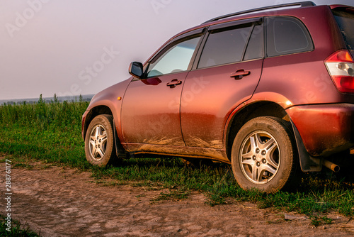 A red crossover stands on the side of a dirt road. Country road along the golden rye field.