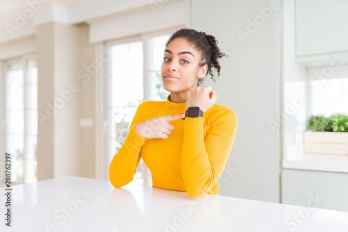 Beautiful african american woman with afro hair wearing a casual yellow sweater In hurry pointing to watch time  impatience  looking at the camera with relaxed expression