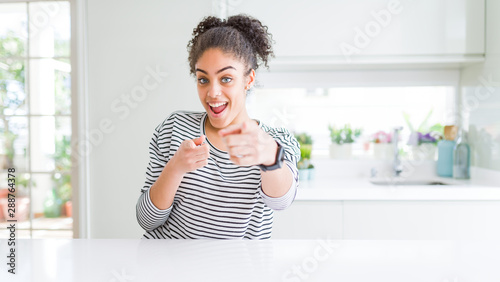 Beautiful african american woman with afro hair wearing casual striped sweater pointing fingers to camera with happy and funny face. Good energy and vibes.