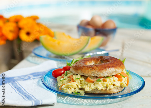 Srambled Egg and Salmon Bagel on glass platee, sunny patio location photo