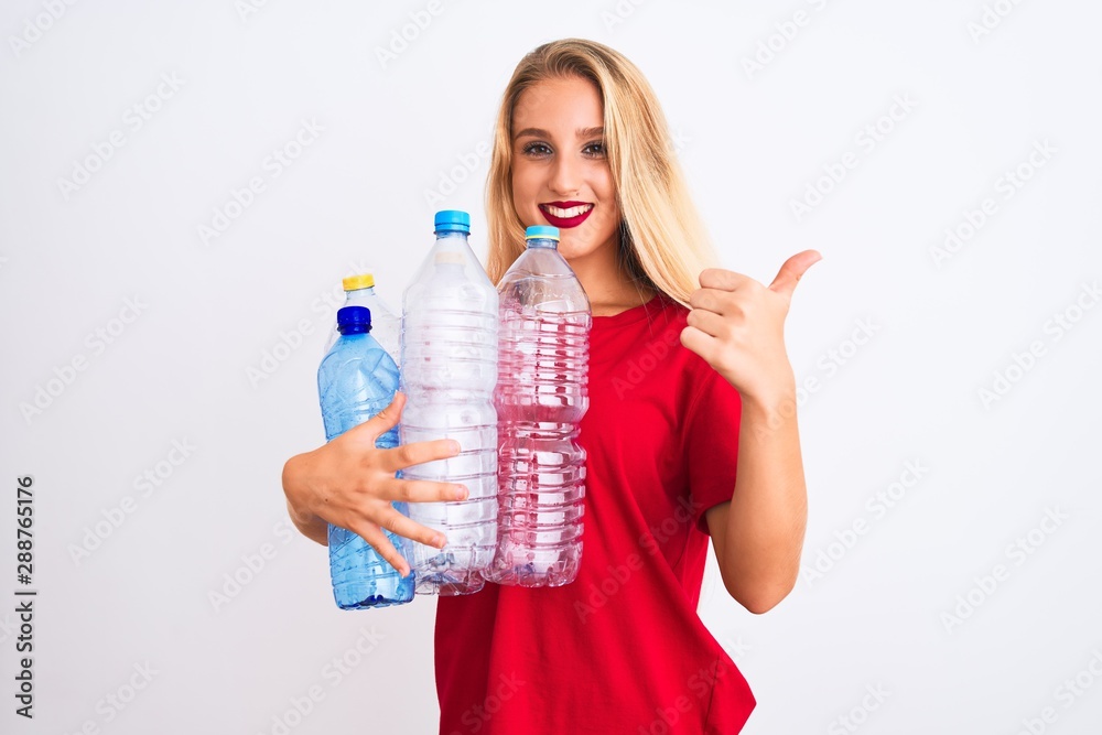 Young beautiful woman recycling plastic bottles standing over isolated white background happy with big smile doing ok sign, thumb up with fingers, excellent sign Young beautiful woman recycling plastic bottles standing over isolated white background happy with big smile doing ok sign, thumb up with fingers, excellent sign