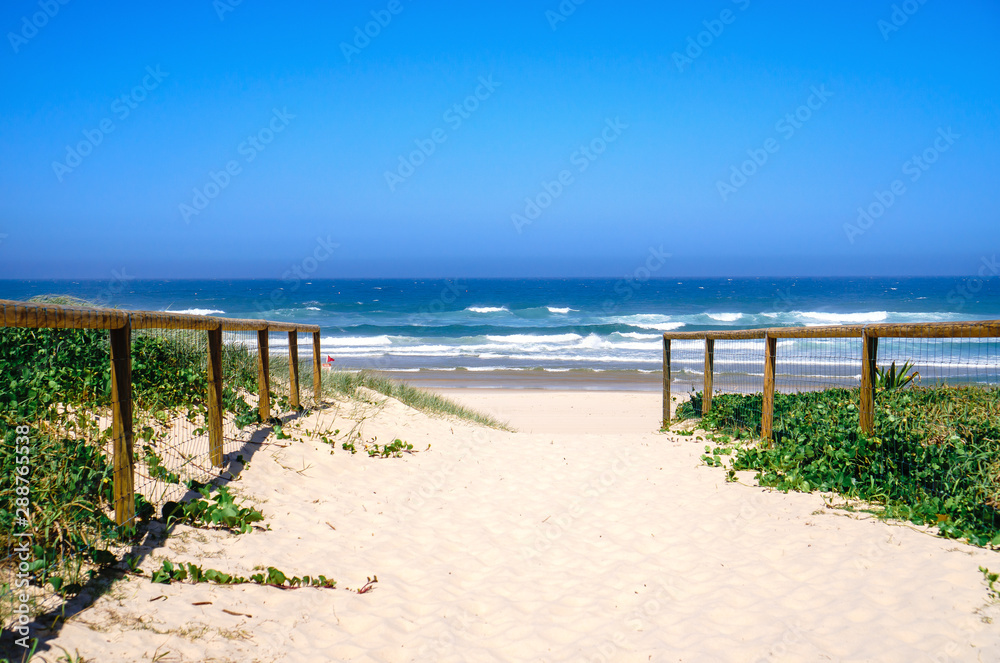 Wide panoramic view of beautiful walking path to the beach and stunning rolling waves of Pacific ocean along wide sandy beach.