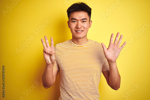 Young asian chinese man wearing t-shirt standing over isolated yellow background showing and pointing up with fingers number eight while smiling confident and happy.