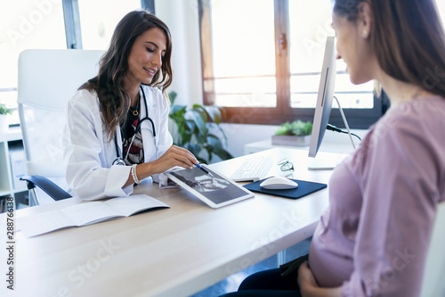 Quadro su tela Pretty young woman gynecologist using digital tablet for showing the ultrasound to her pregnant patient in the clinic