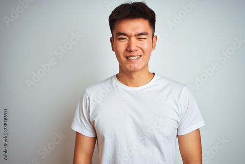 Young asian chinese man wearing t-shirt standing over isolated white background winking looking at the camera with sexy expression, cheerful and happy face.