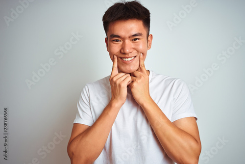 Young asian chinese man wearing t-shirt standing over isolated white background Smiling with open mouth, fingers pointing and forcing cheerful smile