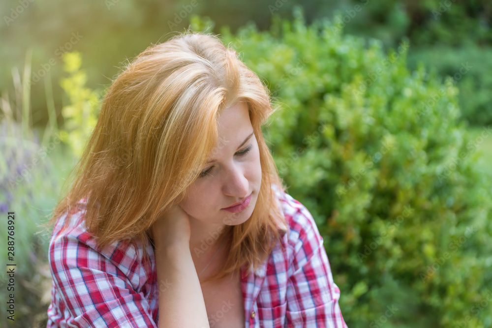 Pensive alone young woman is posing at the garden.  Horizontally. 