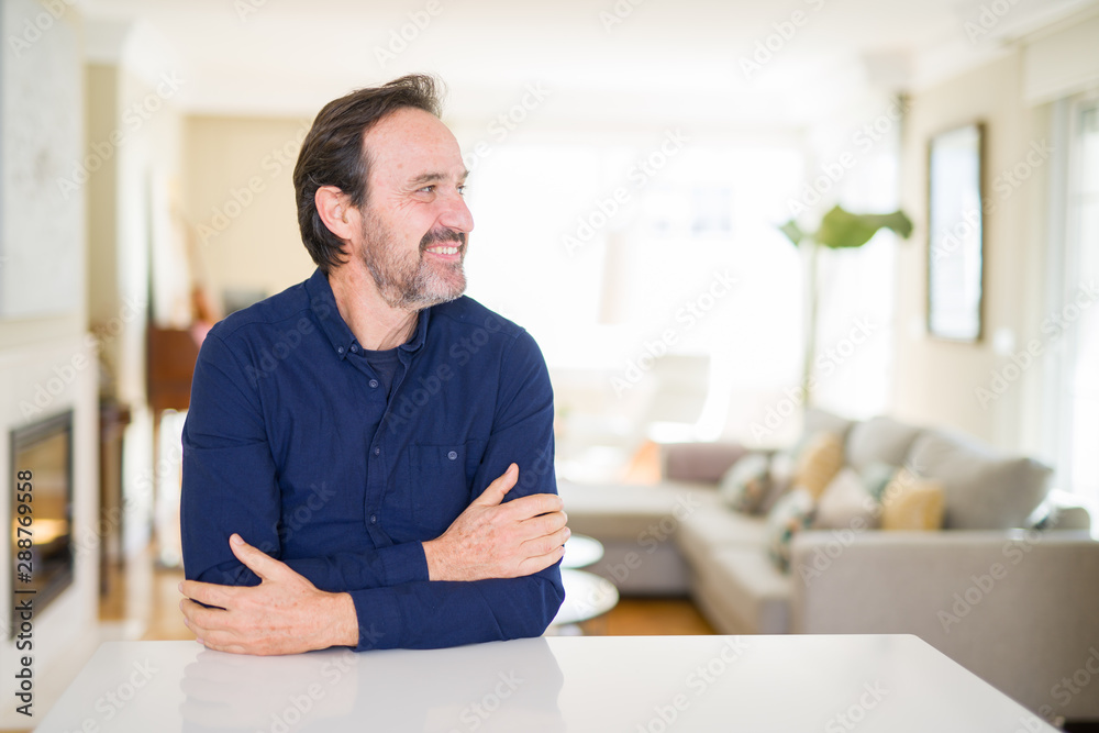 Handsome middle age man at home looking away to side with smile on face, natural expression. Laughing confident.