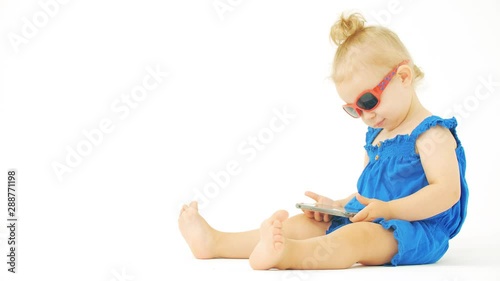 Focused baby girl wearing sunglasses watches movie or cartoon on a smartphone photo