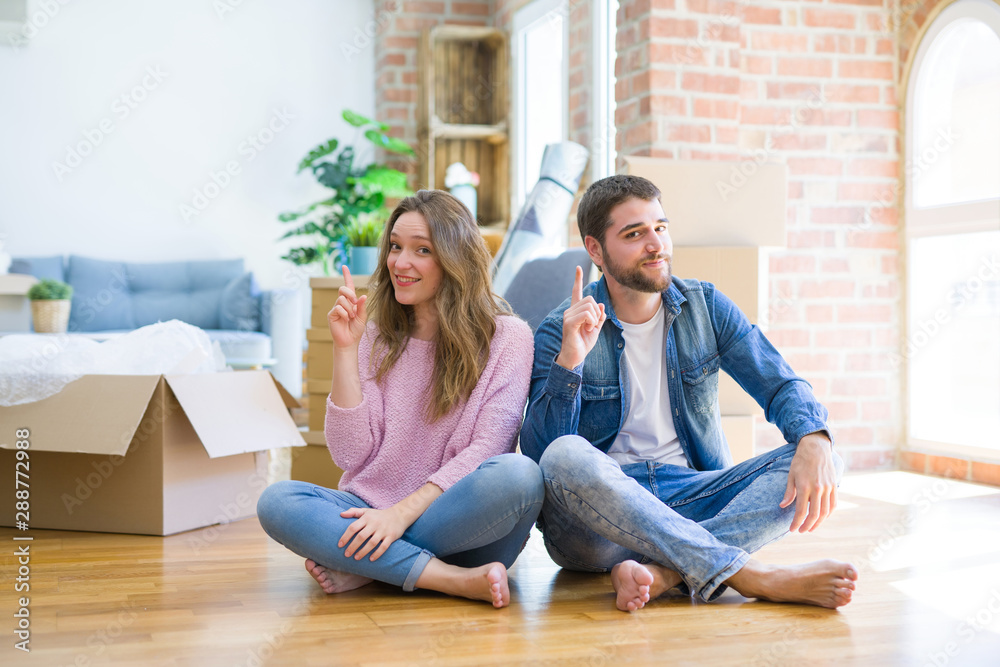 Young beautiful couple moving to a new house sitting on the floor pointing finger up with successful idea. Exited and happy. Number one. Young beautiful couple moving to a new house sitting on the floor pointing finger up with successful idea. Exited and happy. Number one.