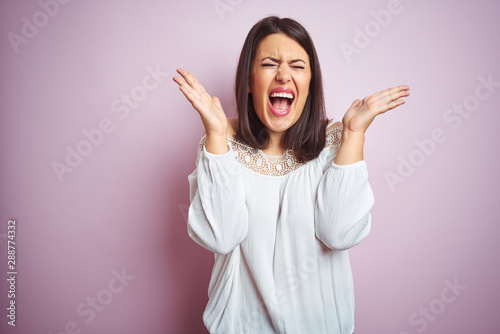 Young beautiful brunette woman over pink isolated background celebrating mad and crazy for success with arms raised and closed eyes screaming excited. Winner concept © Krakenimages.com