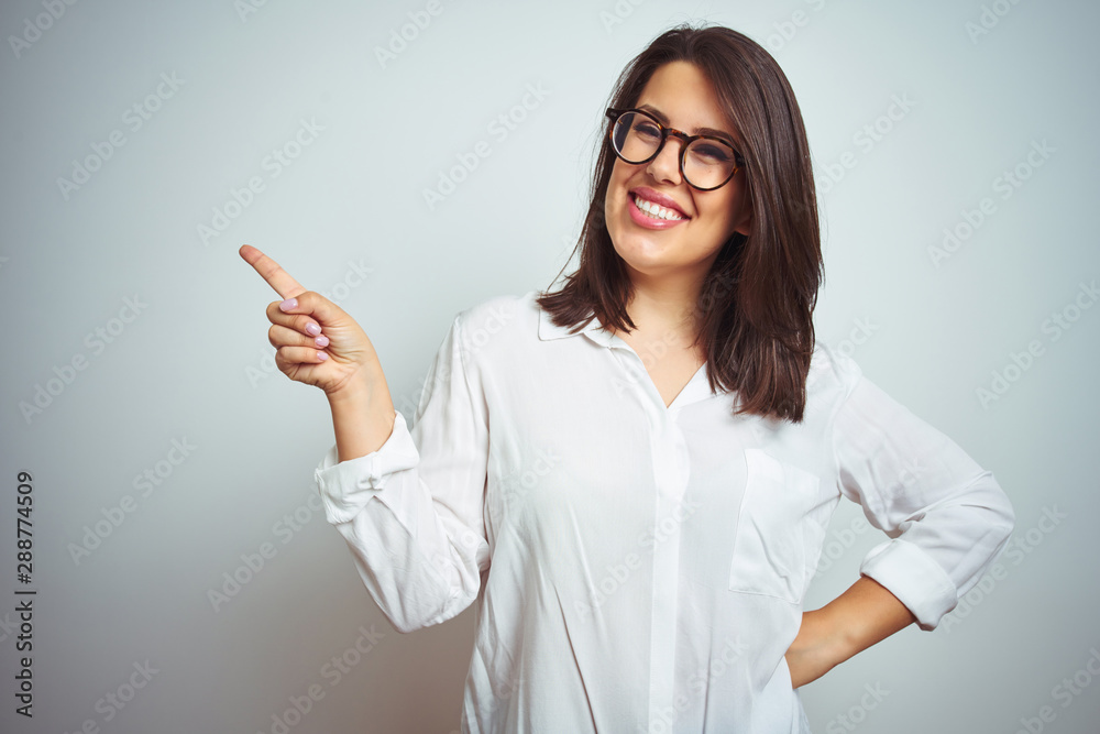 Young beautiful business woman wearing glasses over isolated background with a big smile on face, pointing with hand and finger to the side looking at the camera. Young beautiful business woman wearing glasses over isolated background with a big smile on face, pointing with hand and finger to the side looking at the camera.
