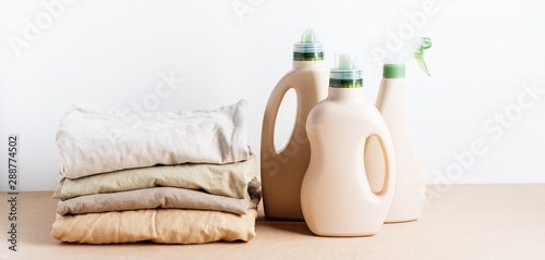 Pile of folded clean clothes with Eco Design bottles packaging for mock up of detergent for laundry on white background. Space for text. Bioorganic product layout.