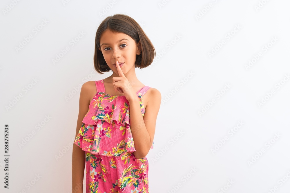 Young beautiful child girl wearing pink floral dress standing over isolated white background asking to be quiet with finger on lips. Silence and secret concept. Young beautiful child girl wearing pink floral dress standing over isolated white background asking to be quiet with finger on lips. Silence and secret concept.