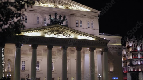 Beautiful facade of the Bolshoi Theater, Moscow. Building was built in 1776. Night time, Main entrance, which is decorated with stucco molding and stunning statues. In the foreground are tree branches