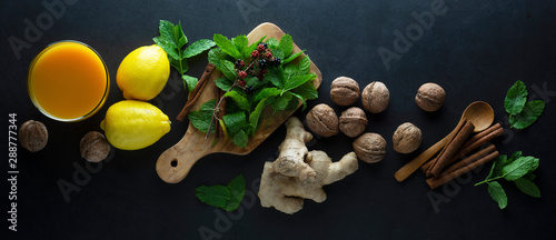 Ginger tea cup with lemons and mint leaves on dark background. Ginger tea, drink ingredients, cold and autumn time. Banner.