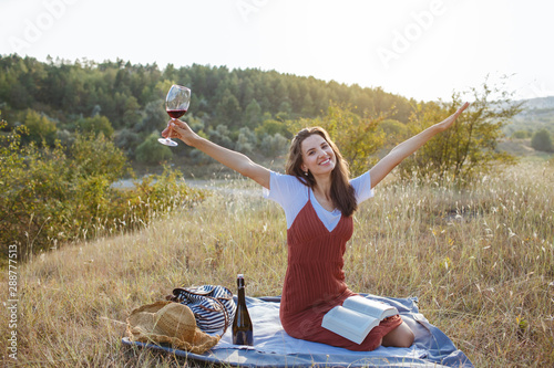 Happy young woman with a glass of wine at sunset.