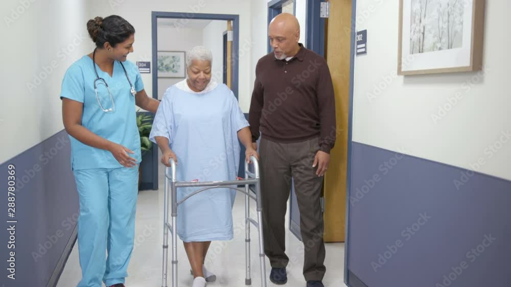 Nurse and husband walk patient down hospital hallway with walker Stock ...