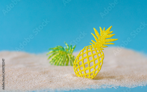 Close-up of bright yellow lace pineapple and green leaves on the sand beach.