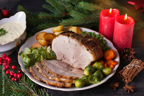 Baked ham with vegetables: potatoes, carrots, brussel sprouts, cabbage, green peas and sauce. Christmas decorations. Dish for Christmas Eve