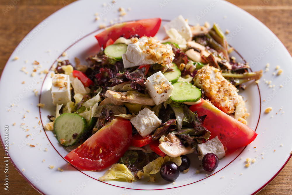 Healthy vegetarian food: tomato, cucumber, lettuce and mushroom salad with feta cheese and walnuts. Close up, horizontal