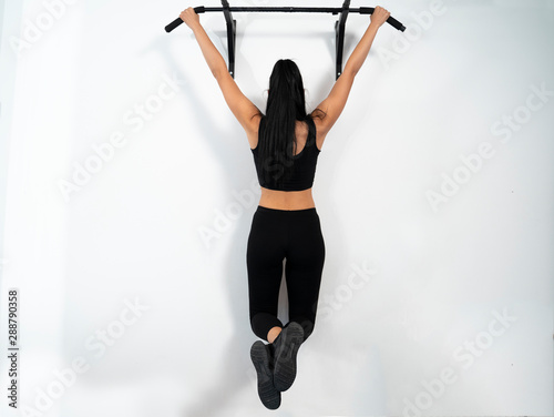 Female hanging on pull ups bar indoors, white wall  photo