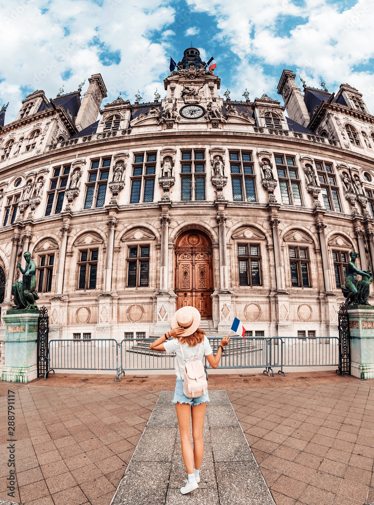 Attractive girl traveler with a cute backpack enjoys the view of the stunning Gothic architecture of the old town Hall in Paris. Your holidays and adventures in Paris