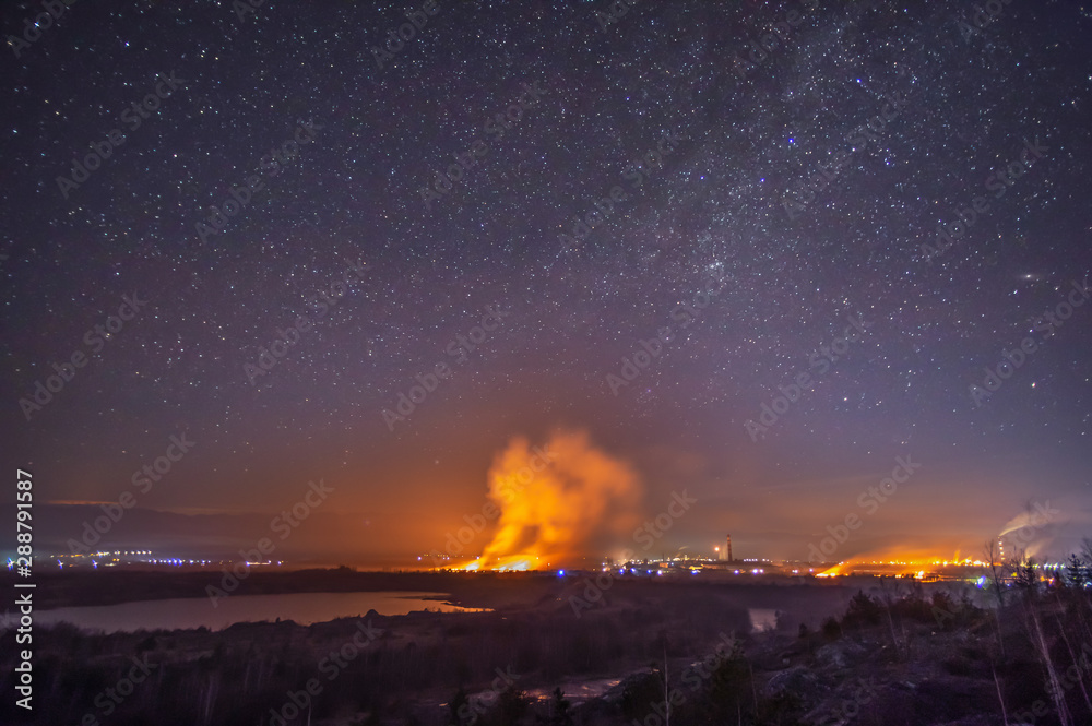 Fire in the field near the city against the background of the starry sky