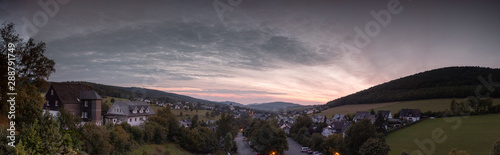 Wide panoramic view over the mountainous village of Grafschaft in the winter sports region of Sauerland, Germany, during sunset with a colourful purple sky © Maarten Zeehandelaar