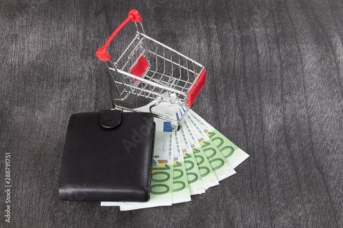 Shopping Cart Full of Cash. Shopping consept, euro money in cart. Shopping cart with euro banknotes and wallet on grey desk. Copy space for text.
