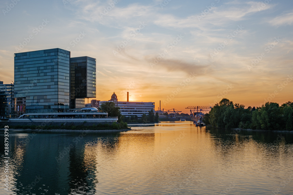 Outdoor scenery of Medienhafen harbour with many boats and yachts anchor at pier, surrounded with modern contemporary architectures during sunset time in Düsseldorf, Germany.