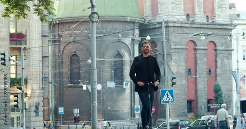 Happy young business man riding to work on electric scooter in beautiful city center. Ecological transport.