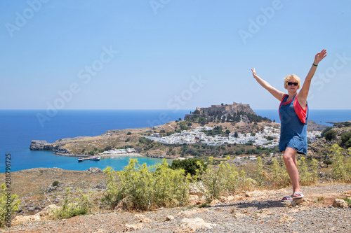  Behind the woman who stands arms outstretched in the distance is the town of Lindos and the medieval castle with the Acropolis.