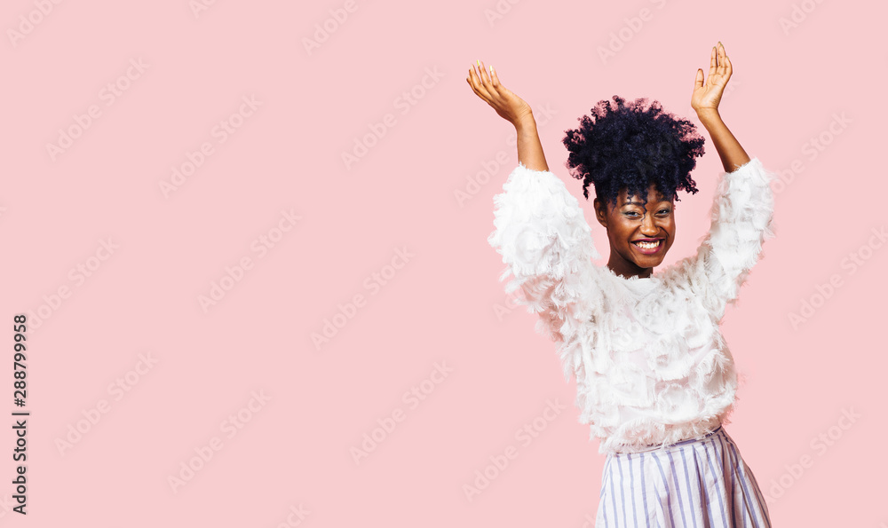 A very happy woman with both arms up against a pink background